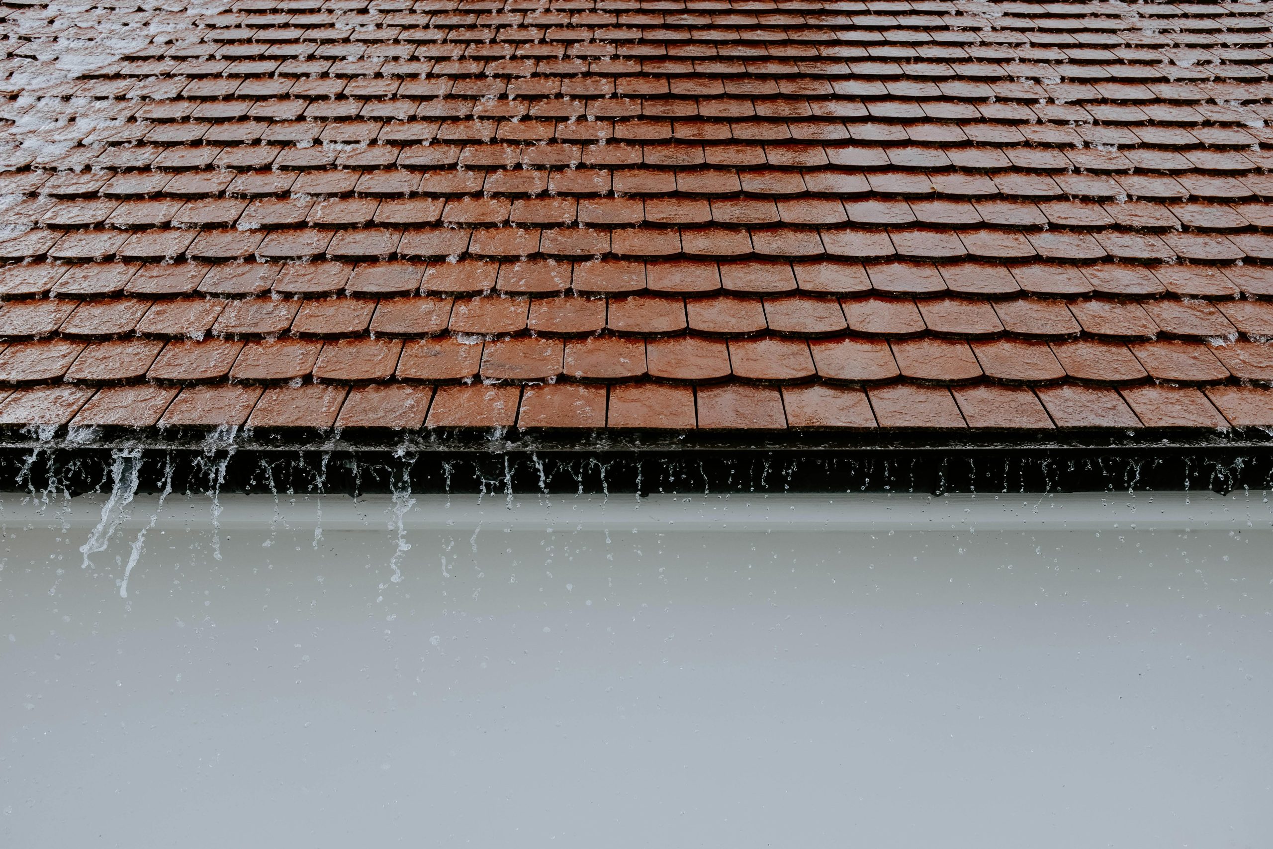Improve Energy Efficiency with Modern Roofing Materials Brown roof tiles with rainwater cascading down, showcasing architectural texture and detail.